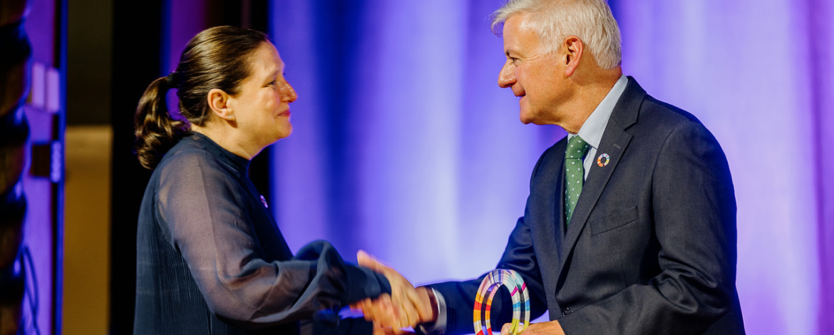 Mann übergibt einer Frau einen Pokal während einer Preisverleihung und gratuliert per Handschlag.
