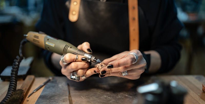 Eine Frau hält einen Schleifer in der Hand und bearbeitet damit Edelmetall.