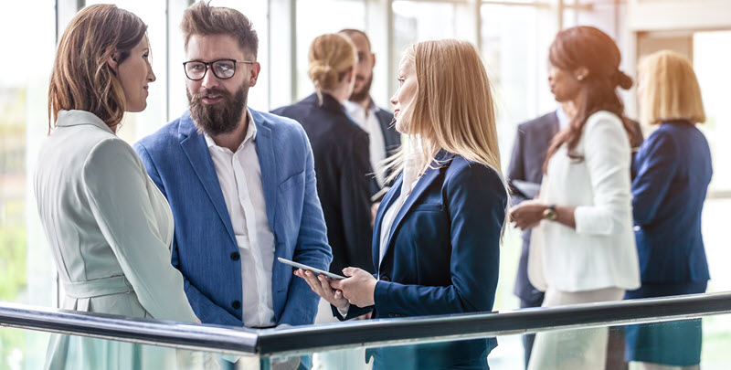 Mehrere Personen im Business Outfit stehen in einer Halle und unterhalten sich.