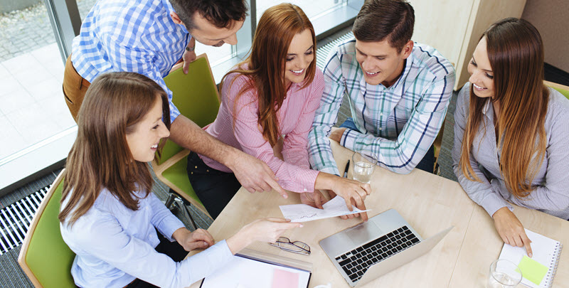 Drei Schülerinnen und ein Schüler sitzen mit einem Laptop an einem Tisch. Ein Lehrer steht hinter ihnen und zeigt ihnen etwas mit seiner rechten Hand. - Link auf Seite: SCHULEWIRTSCHAFT-PREIS 2025: Berufliche Orientierung gemeinsam neu denken – Start der Gründungswoche Deutschland