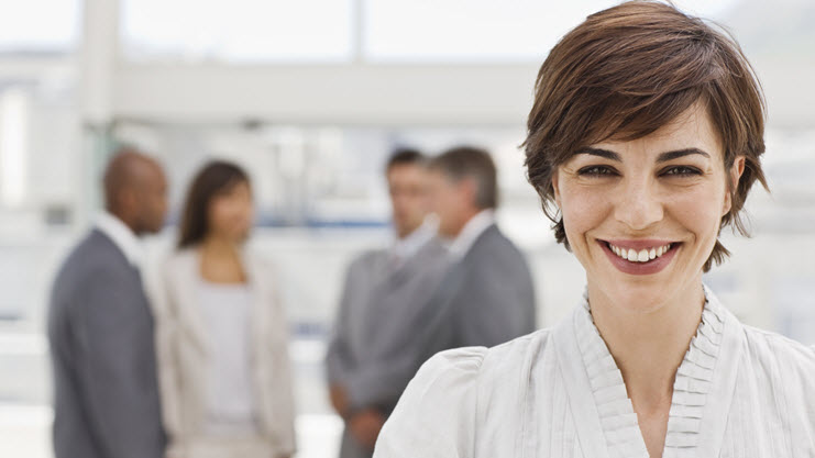 Junge lächelnde Frau vor einer Gruppe Personen in Business Outfits im Hintergrund