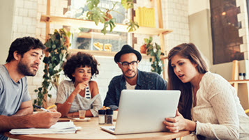 Gruppe junger Menschen sitzen gemeinsam mit Laptop und Dokumenten am Tisch in einem Café