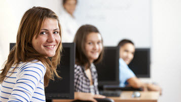 Schülerinnen in einem Klassenraum mit Computern drehen sich um und lächeln