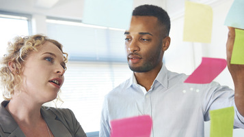 Zwei Menschen stehen vor einer Wand und kleben Post-its darauf