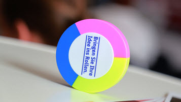 Bild zeigt kreisförmigen Gründungswoche-Stift mit den 3 Farben Pink, Blau und Gelb