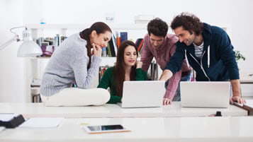 Grupper junger Menschen an einem Schreibtisch schauen auf Laptop