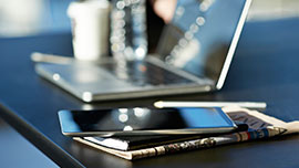 Smartphone und Laptop liegen auf einem Schreibtisch; Link zur Seite mit den aktuellen Meldungen