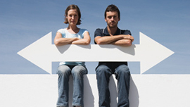 Eine Frau und ein Mann sitzen nebeneinander und halten einen Pfeil, der in zwei gegensätzliche Richtungen zeigt.