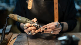 Eine Frau hält einen Schleifer in der Hand und bearbeitet damit Edelmetall.