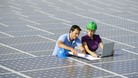 Ein Mann und eine Frau mit Schutzhelmen arbeiten an einem Solarfeld.